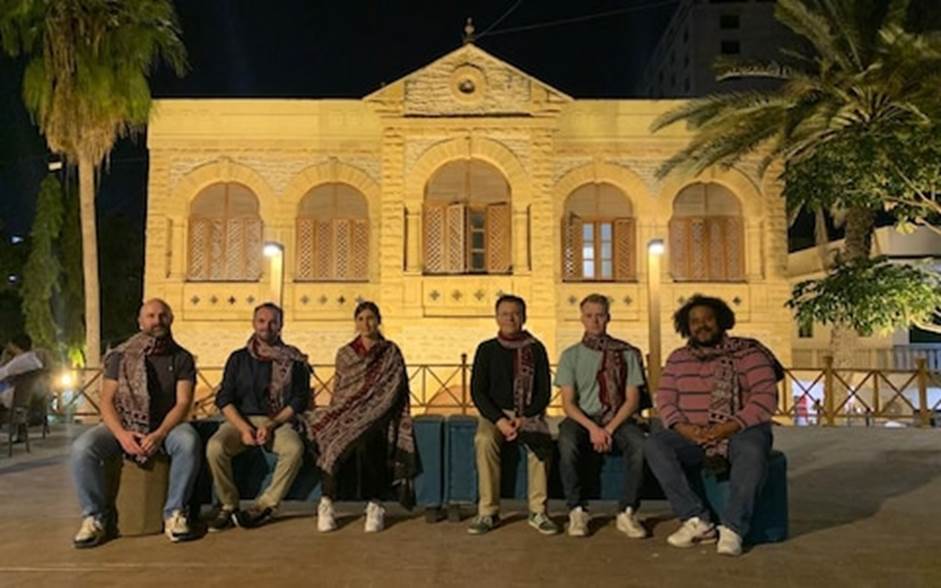 A group of people sitting on a bench in front of a building Description automatically generated
