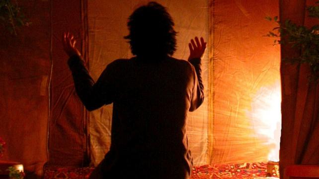 A person praying in front of a light Description automatically generated