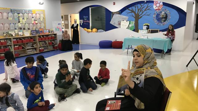 A person in a headscarf pointing at a group of children Description automatically generated with low confidence