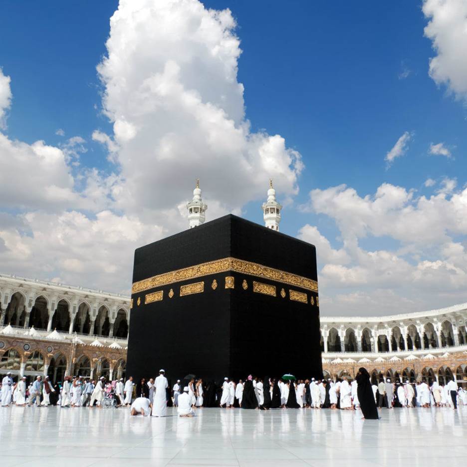 A group of people in white robes with Kaaba in the background Description automatically generated with low confidence
