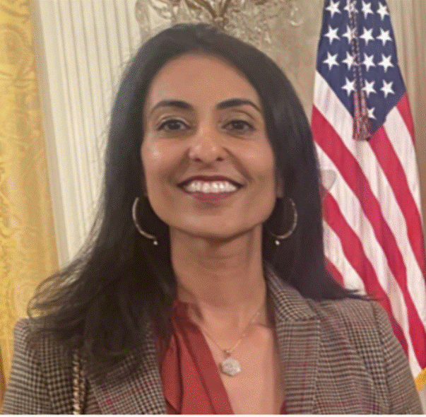 A person smiling in front of a flag Description automatically generated