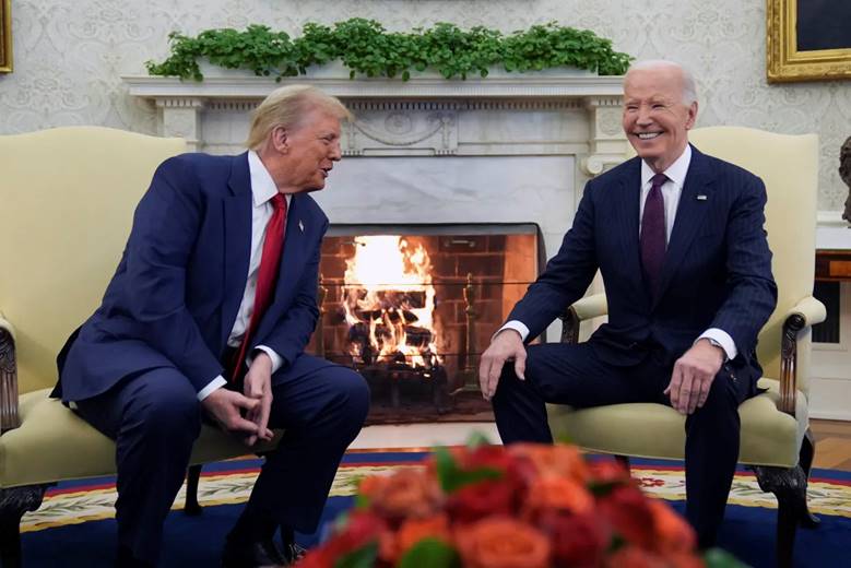 Two men in suits sitting in front of a fireplace Description automatically generated