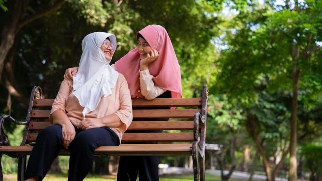 Two women sitting on a bench Description automatically generated