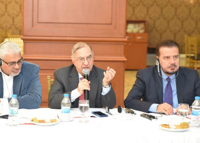 A group of men sitting at a table talking into a microphone Description automatically generated