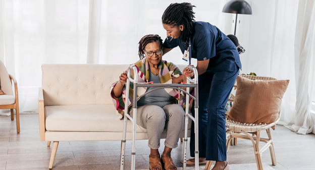 A nurse helping a person to walk on a walker Description automatically generated