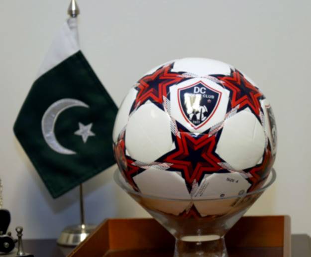 A football ball in a glass cup next to a flag Description automatically generated