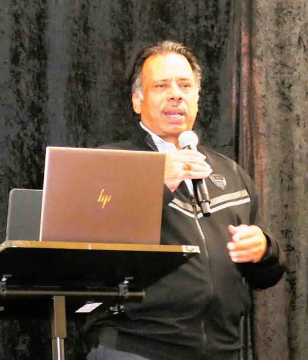 A person standing at a podium with a microphone and a computer Description automatically generated