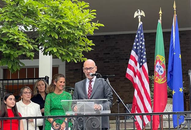 A person standing at a podium with a microphone and people behind him Description automatically generated