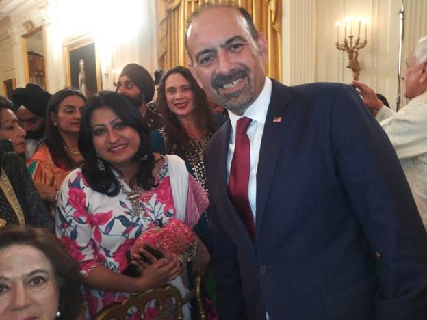 A person in a suit and tie smiling with a group of people in the background Description automatically generated
