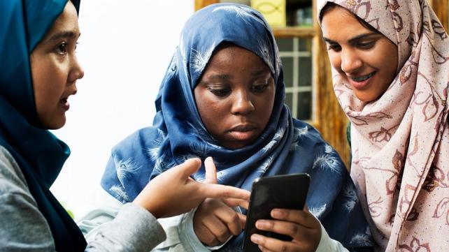 A group of women looking at a phone Description automatically generated