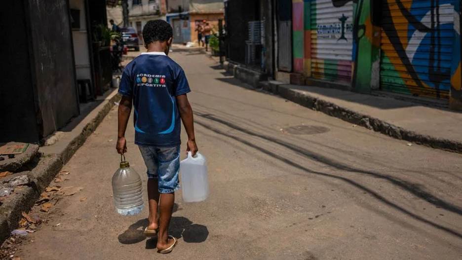 A person carrying two plastic jugs on a street Description automatically generated