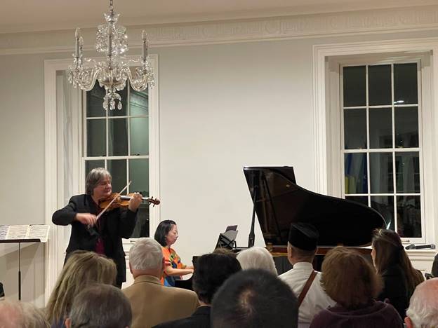 A person playing violin in front of a crowd of people Description automatically generated